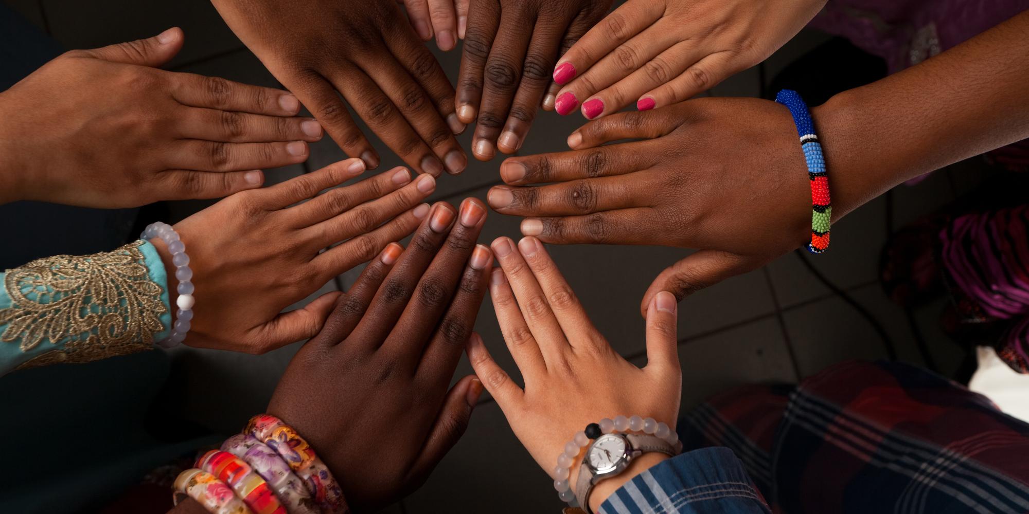 A group of women's hands touching at the fingertips in a circle. 