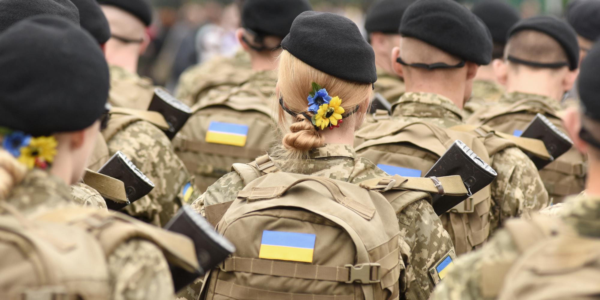 Ukrainian soldiers marching, backs to their camera, female soldier in centre