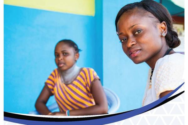 two young women look to camera, sat together, blue background