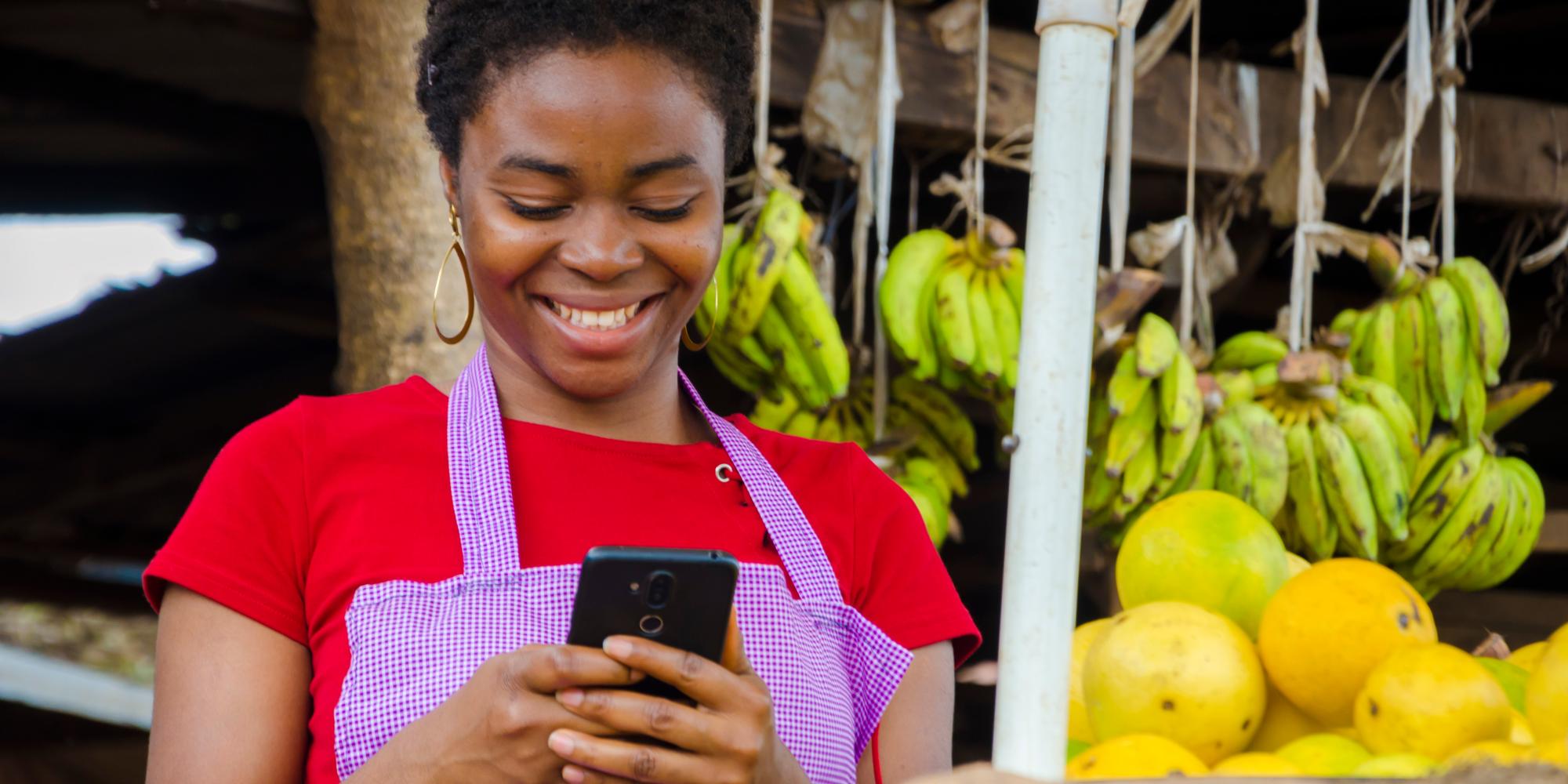 Nigerian woman working at market uses mobile phone