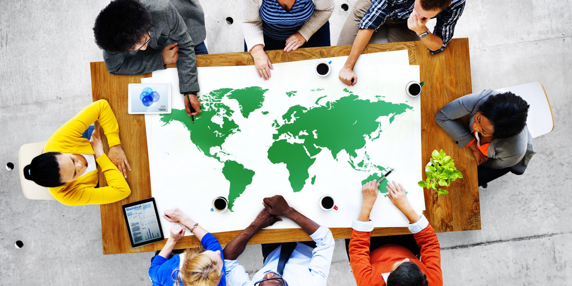 Group of individuals working round a table featuring map of the world