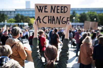 Protestor stands with her back to camera, holding sign that reads "We Need a Change" at a climate change protest